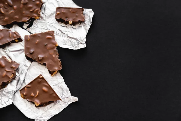 Top view of milk chocolate on foil on black background — Photo de stock