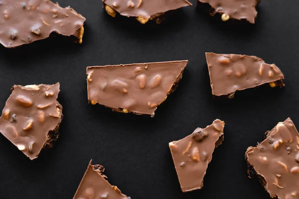 Top view of milk chocolate pieces with nuts on black background — Stock Photo