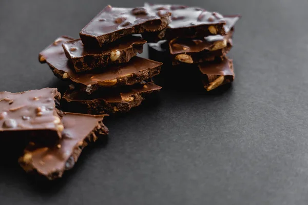 Close up view of tasty milk chocolate with nuts on black background — Fotografia de Stock