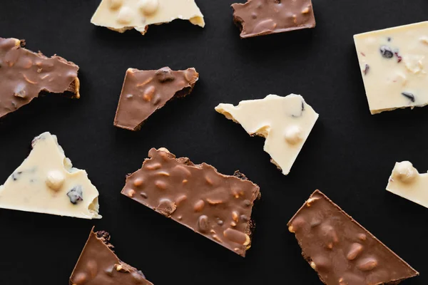 Top view of pieces of milk and white chocolate on black background — Stockfoto