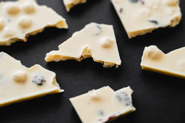 Close up view of white chocolate with nuts and raisins on black background — Stock Photo