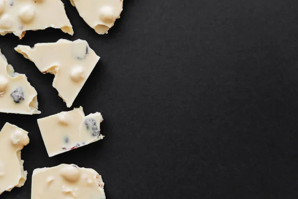 Top view of white chocolate with raisins and nuts on black background with copy space — Stock Photo