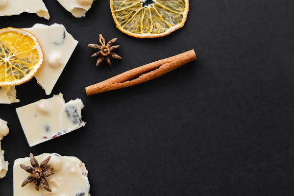 Vue de dessus du chocolat blanc, des épices et des tranches d'orange sèches sur fond noir — Photo de stock