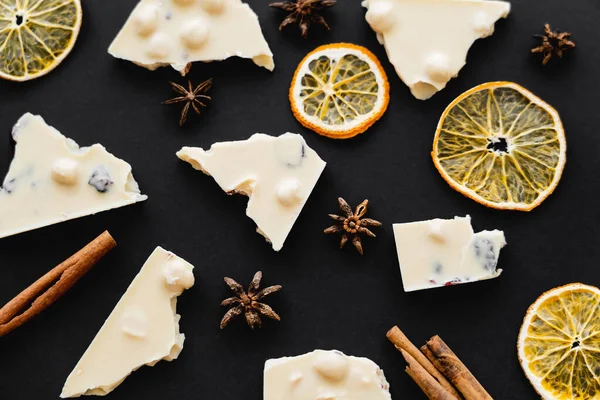 Top view of slices and dry orange slices near white chocolate on black background — стоковое фото