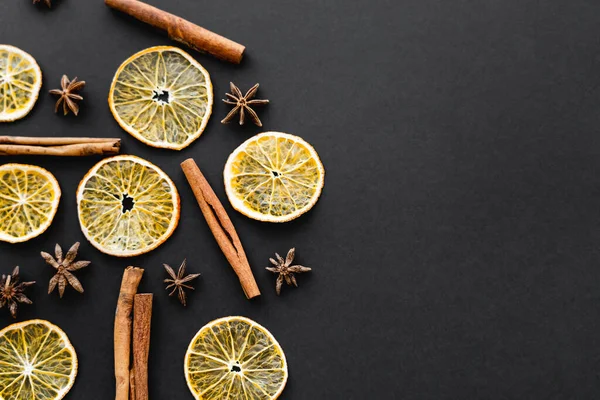 Vue de dessus de l'anis sec, des tranches d'orange et des bâtonnets de cannelle sur fond noir — Photo de stock