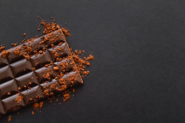 Draufsicht auf dunkle Schokoladenriegel mit Kakaopulver auf schwarzem Hintergrund mit Kopierraum — Stockfoto