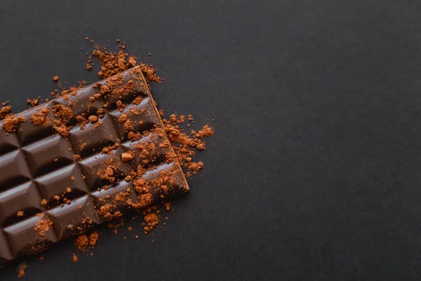 Top view of dark chocolate bar with cocoa powder on black background  with copy space — Stockfoto