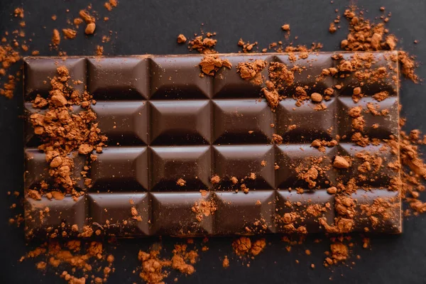 Vista superior do cacau natural na barra de chocolate no fundo preto — Fotografia de Stock