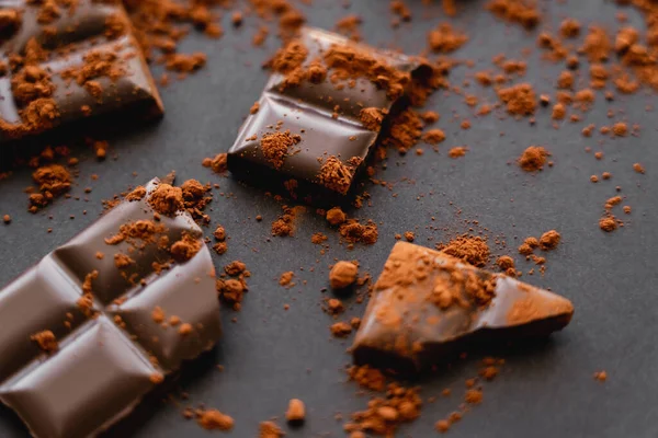 Close up view of dry cocoa powder on chocolate pieces on black background — стоковое фото