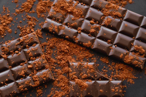 Top view of natural cocoa and chocolate bars on black background — Stockfoto