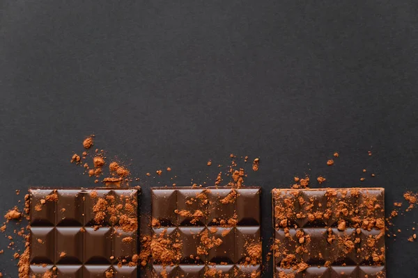 Top view of chocolate bars with dry cocoa powder on black surface — Stockfoto