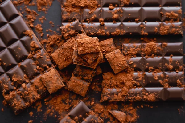 Vista superior de polvo seco de coca sobre chocolate desenfocado sobre fondo negro - foto de stock