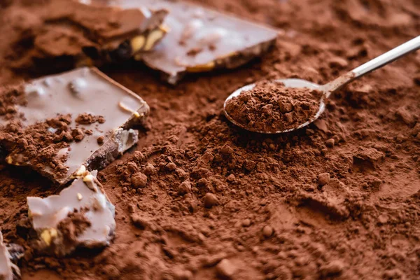 Nahaufnahme eines Löffels in der Nähe von Schokolade mit Nüssen auf trockenem Kakao — Stockfoto