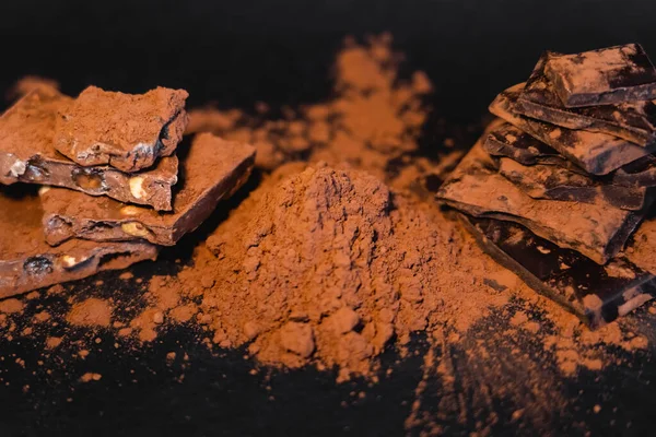 Vue rapprochée du cacao naturel en poudre et du chocolat sur fond noir — Photo de stock