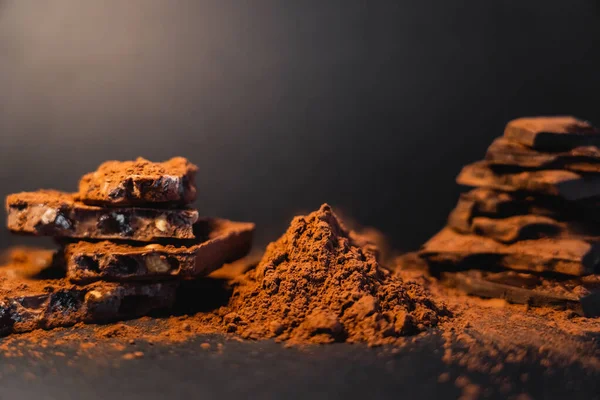 Close up view of dry cocoa and blurred chocolate on black background — Photo de stock
