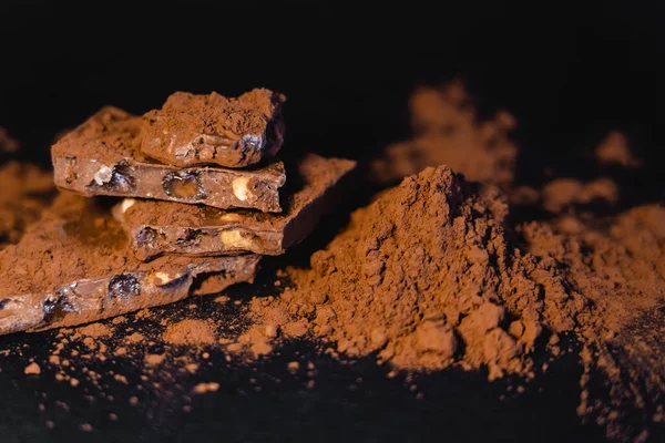 Nahaufnahme von Kakao und Vollmilchschokolade mit Nüssen auf schwarzem Hintergrund — Stockfoto