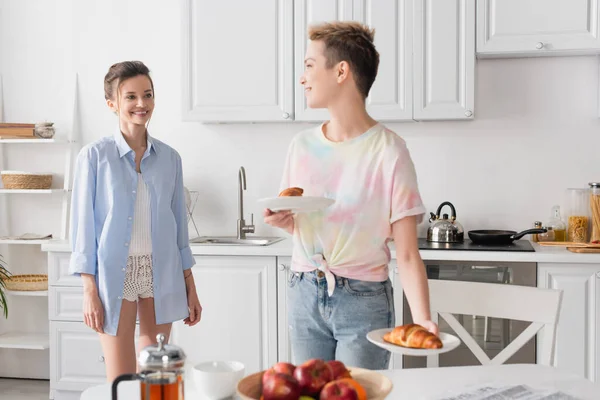 Pansexual person holding plates with croissants near happy partner — Fotografia de Stock