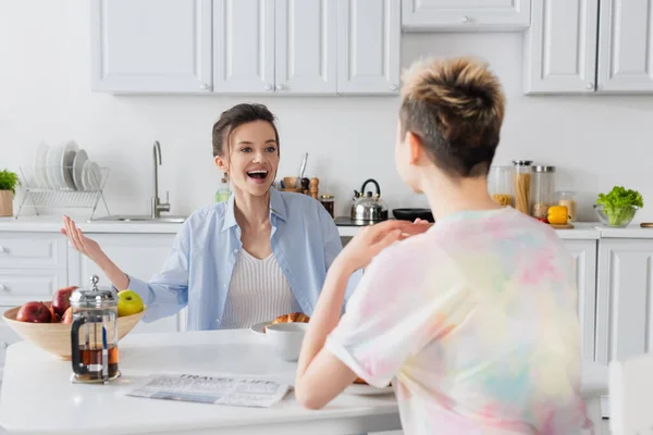 Excited pansexual person laughing and gesturing near blurred partner during breakfast — стоковое фото