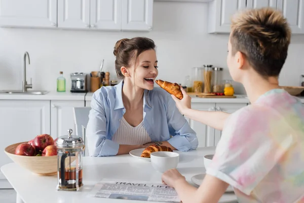 Pangender person feeding partner with croissant during breakfast — Stock Photo