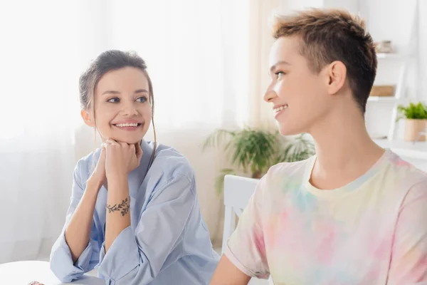 Happy pangender couple smiling at each in kitchen - foto de stock