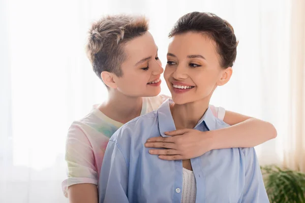 Young bigender person with closed eyes embracing smiling partner — стоковое фото