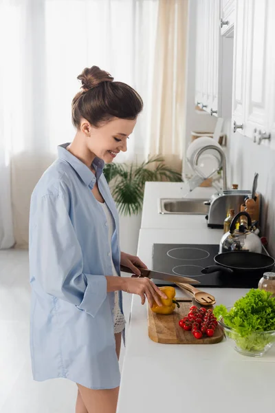 Side view of smiling brunette woman cutting bell pepper near cherry tomatoes — Stock Photo