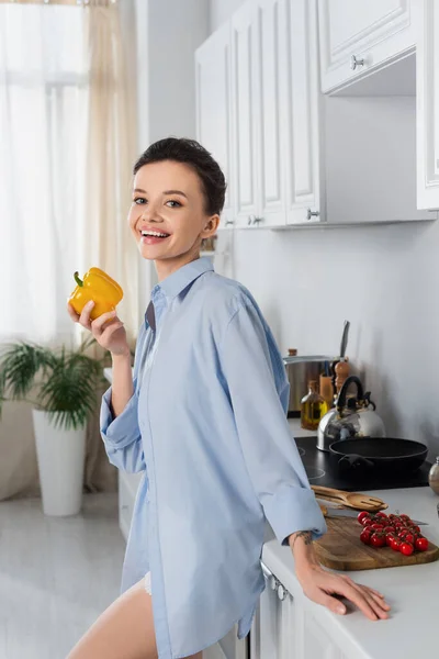 Smiling woman holding bell pepper and looking at camera near fresh cherry tomatoes — Stock Photo