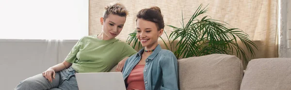 Joyful pangender people sitting on couch and watching movie on laptop, banner - foto de stock