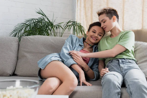 Young bigender person with closed eyes sitting on sofa near cheerful partner — Stockfoto