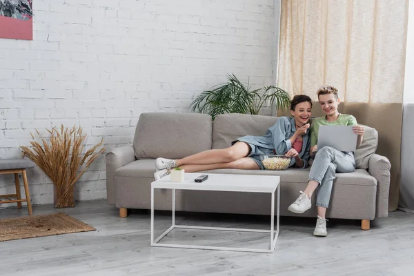 Fröhliche Pangender-Liebhaber sehen Film auf Laptop im modernen Wohnzimmer — Stockfoto