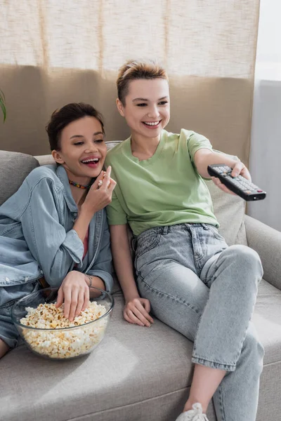 Persona allegra bigender cliccando canali tv vicino amante con ciotola di popcorn — Foto stock