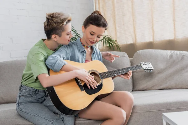 Young musician teaching pansexual partner to play guitar at home — Stockfoto
