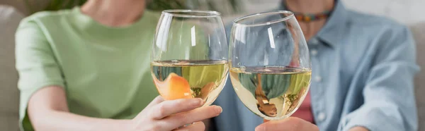 Vue partielle de flou couple pangender cliquetis verres avec vin blanc, bannière — Photo de stock