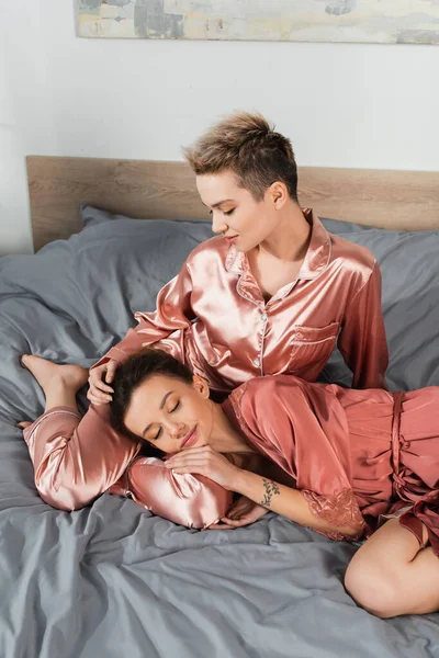 Pansexual person sleeping near lover sitting on bed in silk pajamas — Photo de stock