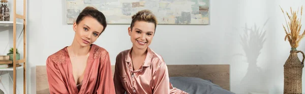 Happy pangender couple in sleepwear looking at camera in bedroom, banner — Stock Photo