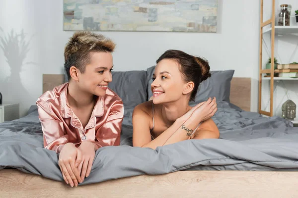 Cheerful pansexual lovers lying on bed and smiling at each other — Fotografia de Stock