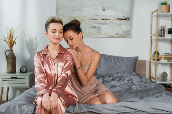 Bigender person with closed eyes sitting on bed near young partner - foto de stock