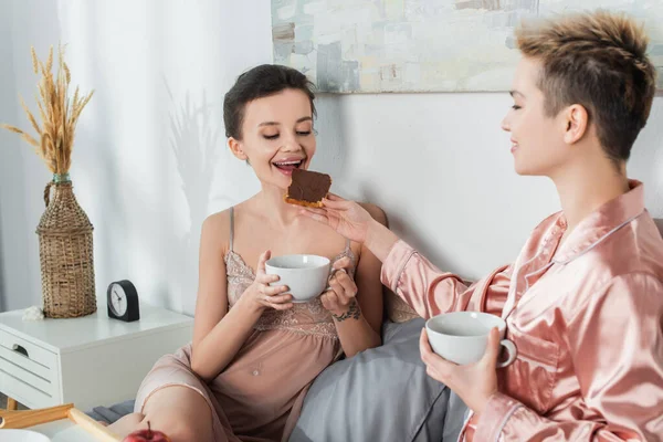 Young bigender person feeding lover with sweet toast bread during breakfast in bedroom — Photo de stock
