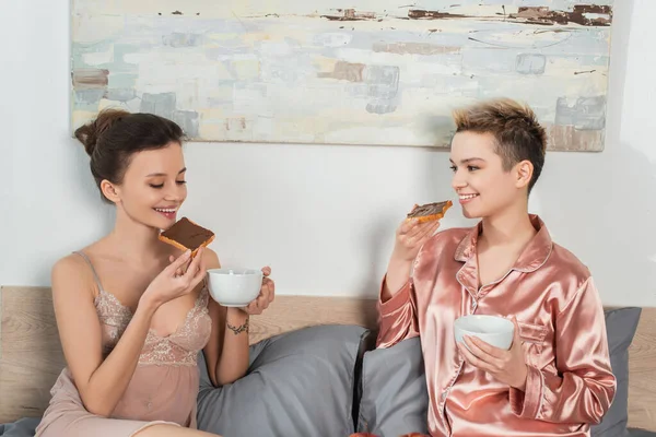 Persone felici pangender bere il tè con pane tostato dolce per la prima colazione in camera da letto — Foto stock