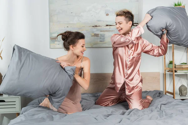 Aufgeregte Pangender mit Kopfkissen, die Spaß haben und im Schlafzimmer kämpfen — Stockfoto