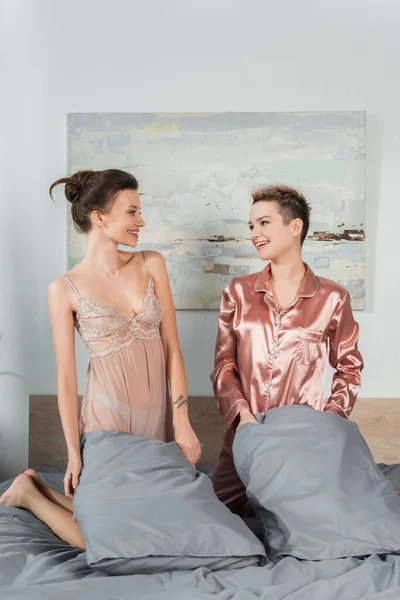 Joyful pansexual lovers holding pillows and smiling at each other in bedroom — Stock Photo