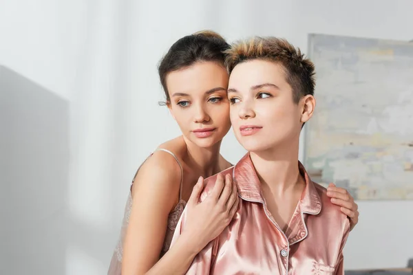 Pangender person hugging shoulders of young partner looking away in bedroom — Foto stock