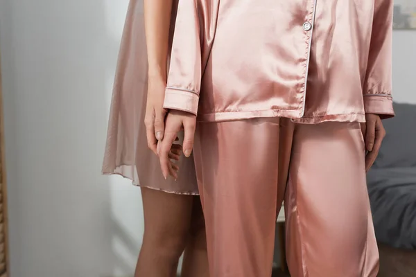 Cropped view of pansexual person in silk pajamas standing near partner in bedroom — Stock Photo