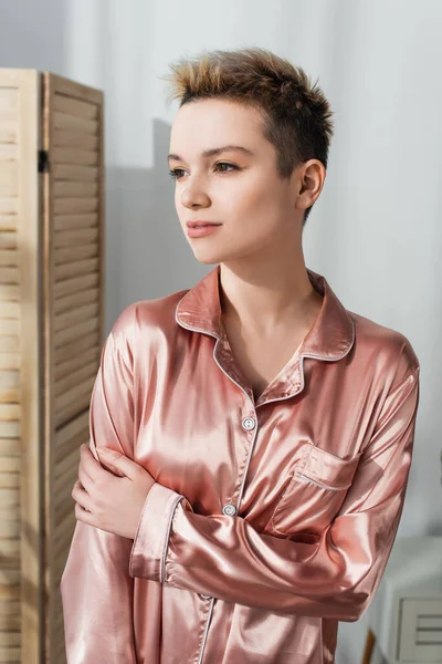 Thoughtful pangender person in silk pajamas looking away at home — Stock Photo