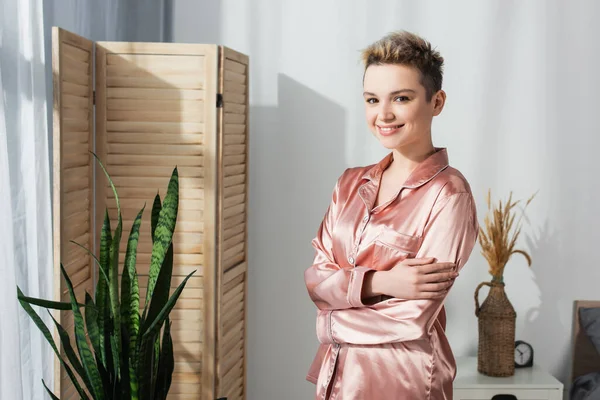 Cheerful pansexual person in silk pajamas standing with crossed arms and looking at camera — Stock Photo