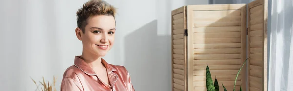 Happy young bigender person with short hair looking at camera at home, banner — Photo de stock