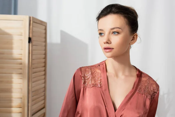 Pretty brunette woman in peignoir looking away at home — Stock Photo