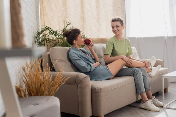 Smiling pansexual people looking at each other while resting on couch on blurred foreground — стоковое фото