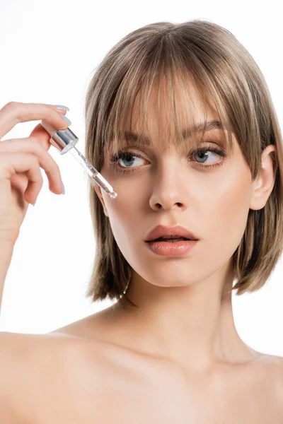 Young woman with bangs looking at pipette with serum isolated on white — Stock Photo