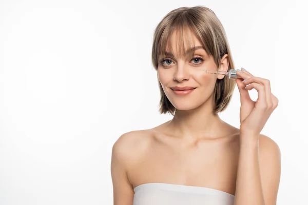 Mujer joven positiva con flequillo aplicando suero aislado sobre blanco - foto de stock